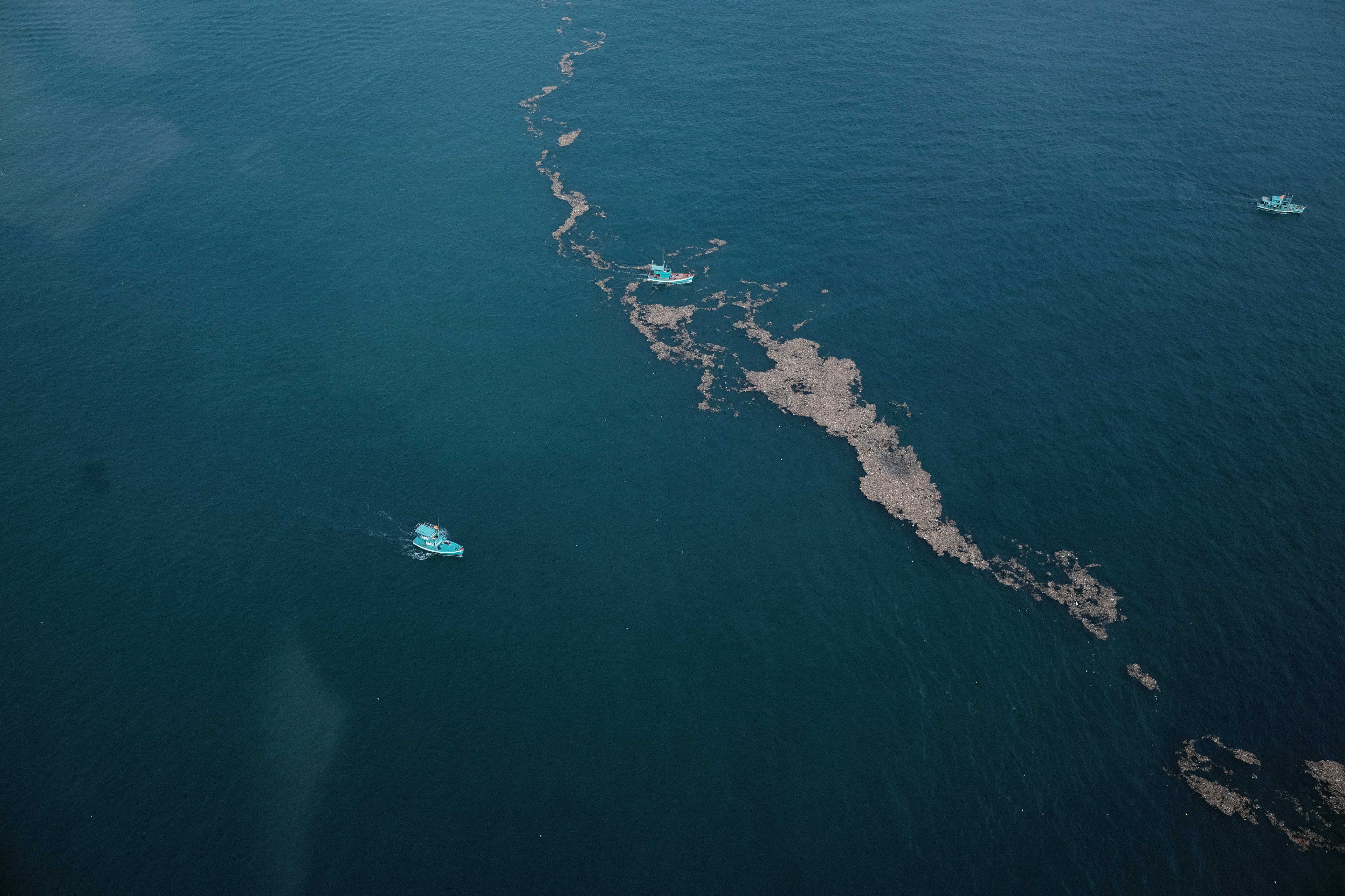 Small boats on blue water beside a long, pale trail, seen from above.