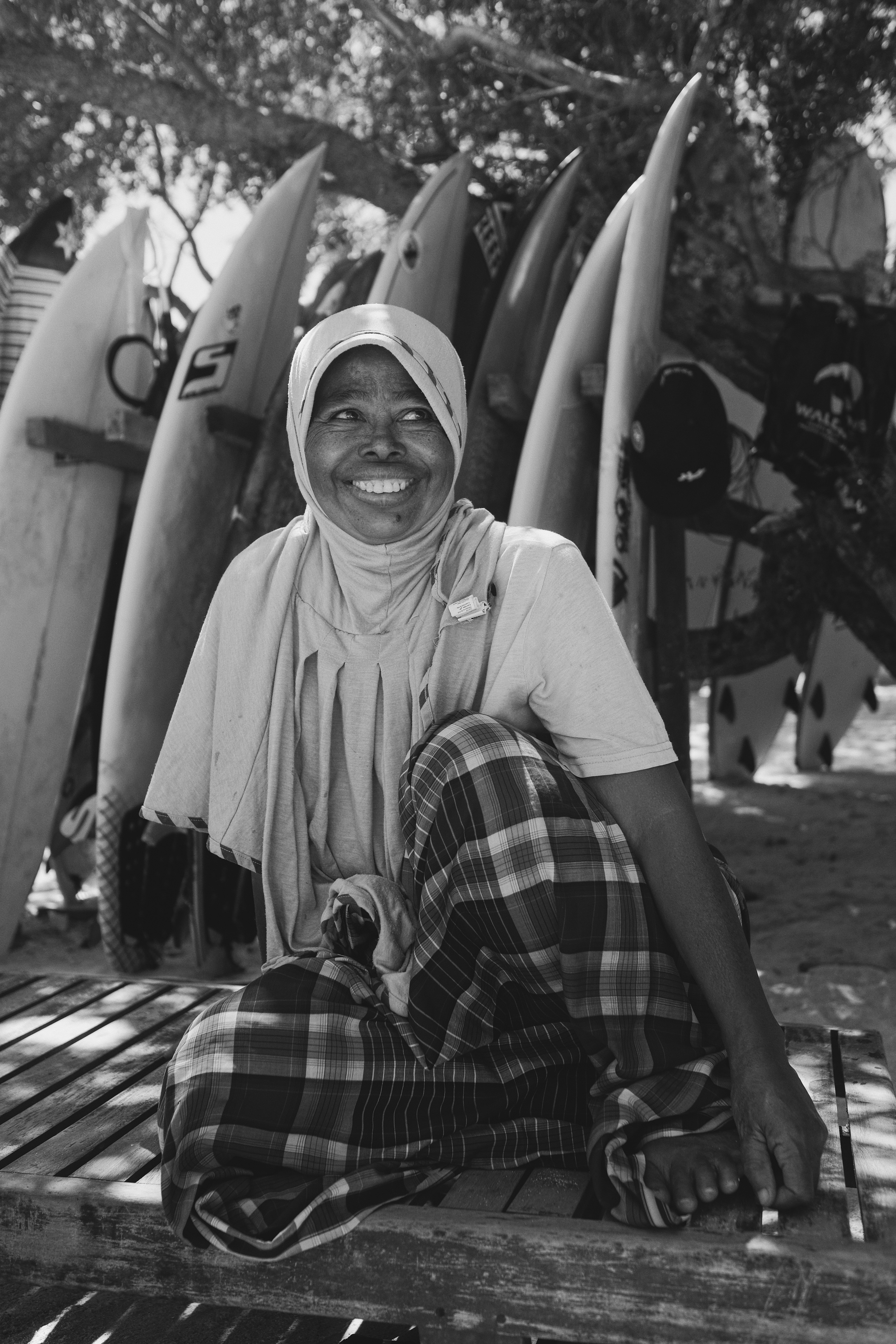 A smiling woman seated in front of surfboards, in black and white.
